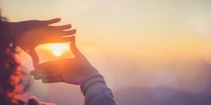 Girl looking through hands at sun to focus on future inspiration.